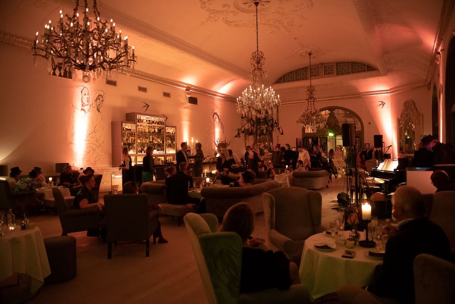 Halloween event with Alice in Wonderland theme in Nimb Bar, Tivoli, Copenhagen. The guests are sitting in green, velvet armchairs and sofas. Some guests are wearing Halloween costumes. Playing cards are hanging from the cystal chandeliers.