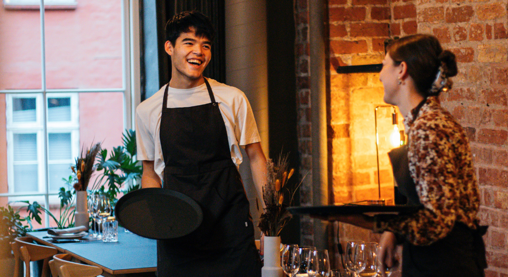 Two smiling waiters setting tables in a restaurant