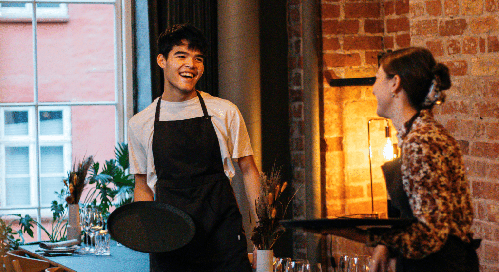Two smiling waiters setting tables in a restaurant