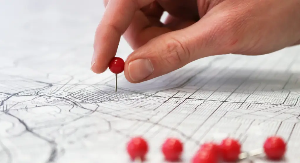 A hand placing a red pin in a map