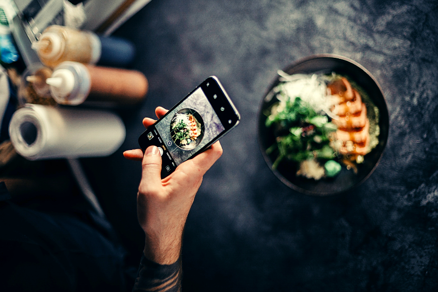 The hand of someone holding a phone over a plate of food to take a picture. 
