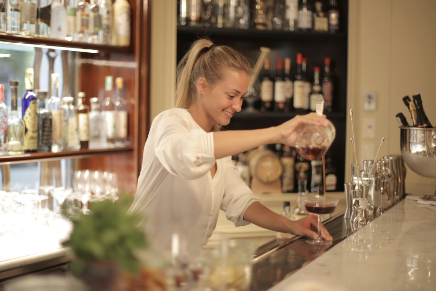 Woman in white shirt pouring a drink from a clear glass bottle. 