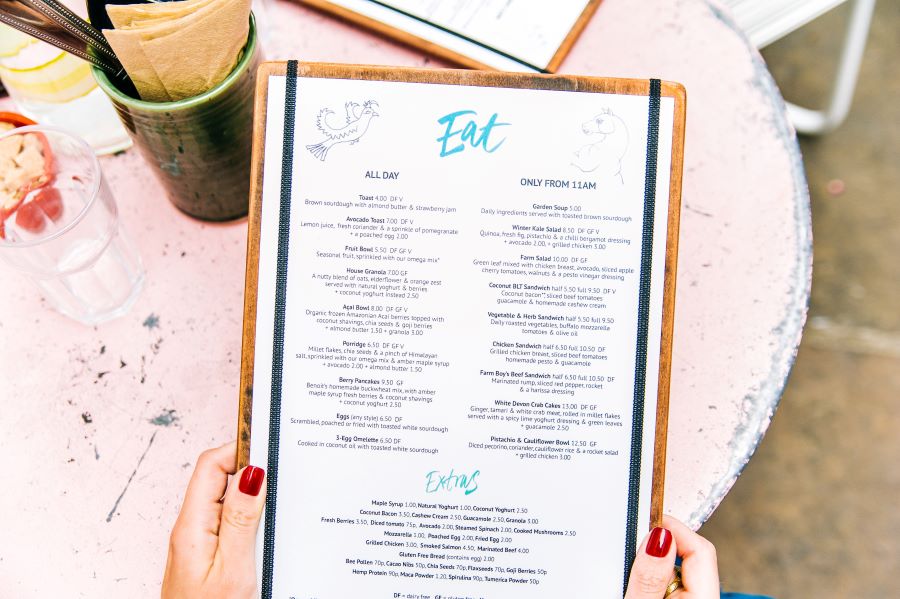 Manicured hands with red nail polish holding a restaurant menu over a white table. 